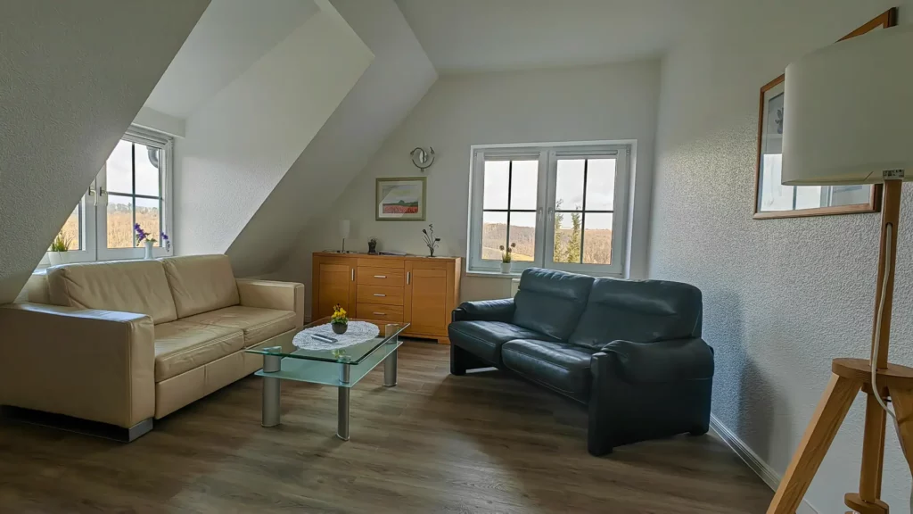 Komfortabel und schick eingerichtetes Wohnzimmer der Ferienanlage Jacqueline mit zwei großen Couchanlagen, einem großen Glastisch, Sideboard, Stehlampe und LCD-Fernseher.