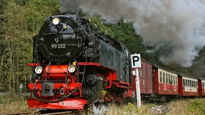 Foto einer historischen Dampflok mit Personenanhängern auf der Schmalspurbahn Richtung Brocken, die durch die Wälder des Harzes fährt